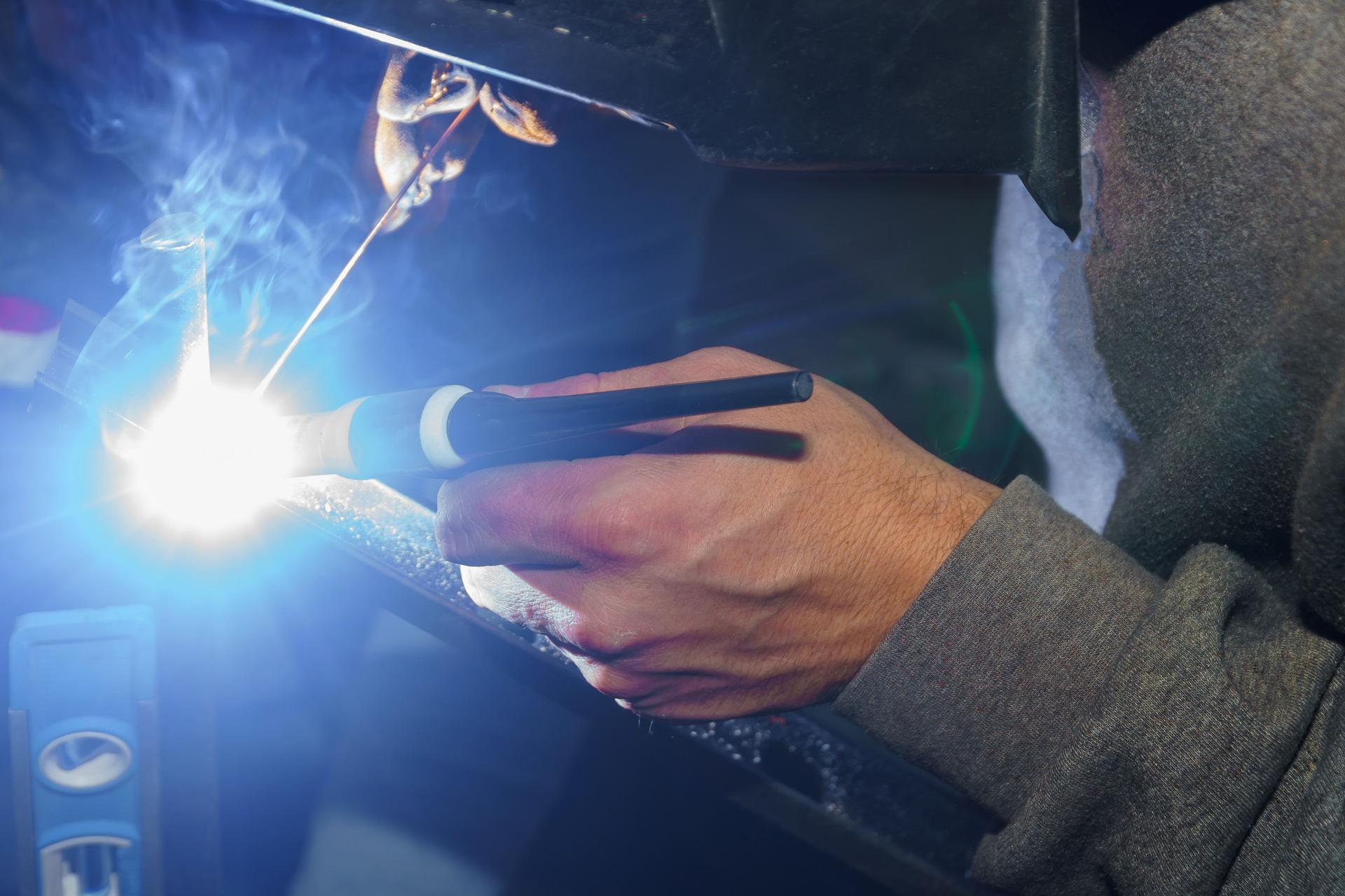 Trabajador en máscara protectora soldadura acero pasamanos en el interior, las chispas volar abajo